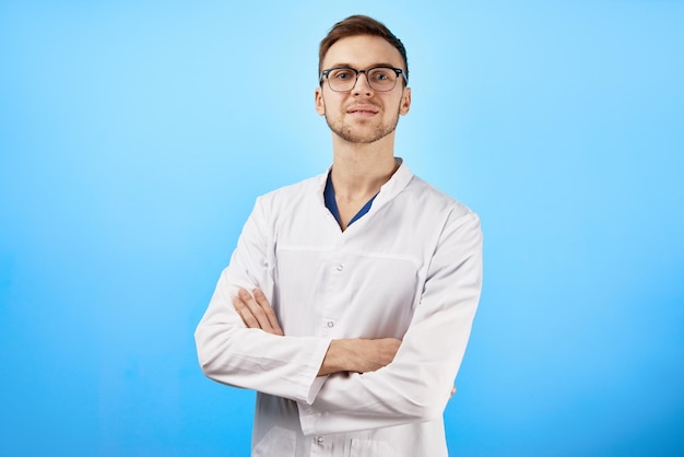 Retrato de um médico caucasiano sorridente em óculos e casaco médico branco isolado em fundo azul