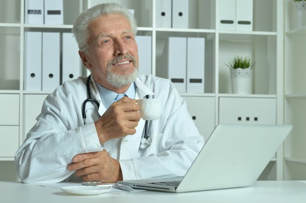 Retrato de um médico idoso com laptop no escritório