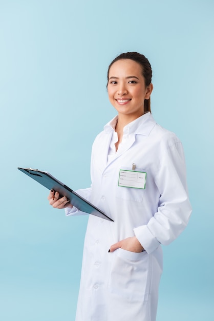 retrato de um médico jovem alegre posando isolado sobre uma parede azul segurando a prancheta.