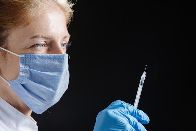 Retrato de um médico ou enfermeiro em uniforme médico e máscara azul protetora com uma seringa em seu ha