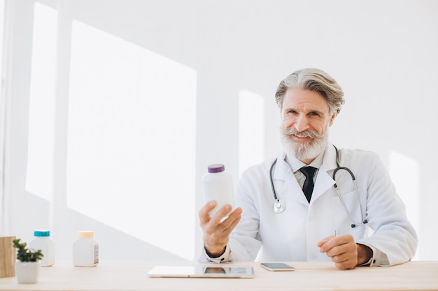 Retrato de um médico sênior segurando um frasco de medicamento em um hospital