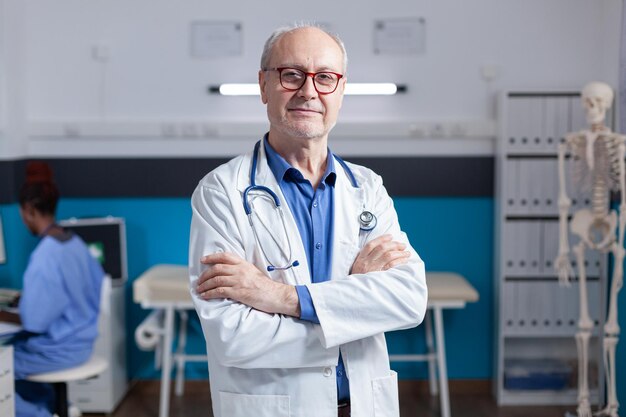 Retrato de um médico sorridente com jaleco branco e estetoscópio em pé com os braços cruzados