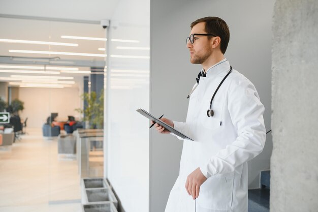 Retrato de um médico sorridente de uniforme em pé no salão da clínica de medicina