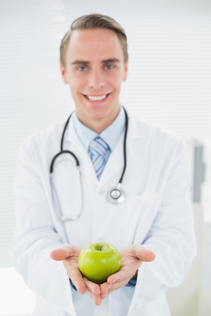 Retrato de um médico sorridente segurando uma maçã verde