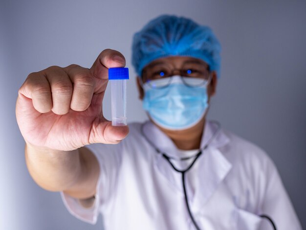 Retrato de um médico usando uma máscara e um chapéu fique segurando um frasco de vacina ou comprimidos vazio. conceito médico e tratamento.