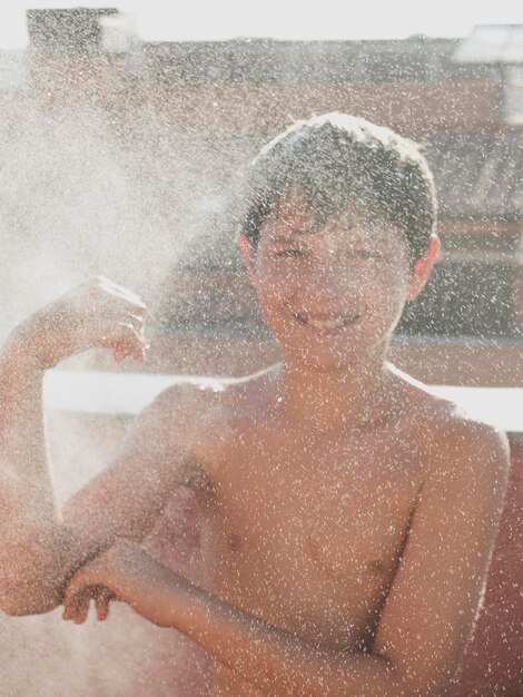 Retrato de um menino adolescente sem camisa tomando banho enquanto está de pé ao ar livre