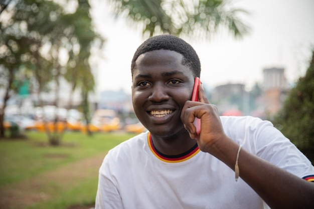 Retrato de um menino africano fazendo uma ligação com seu smartphone ao ar livre em um parque público