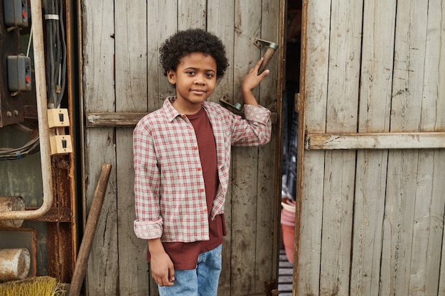 Retrato de um menino africano sorrindo para a câmera em pé perto da porta de madeira ao ar livre