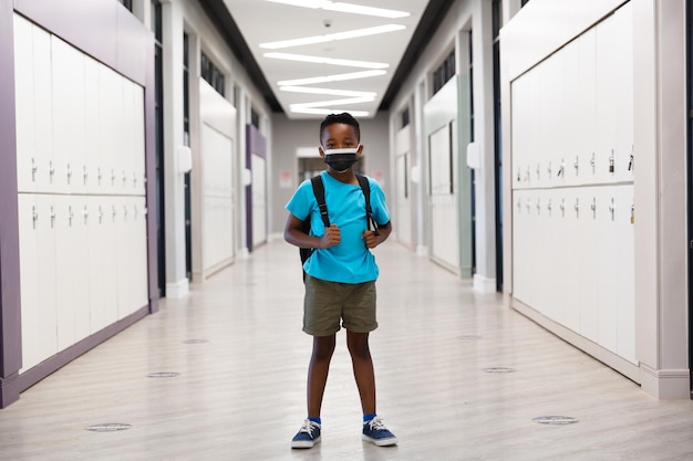 Retrato de um menino afro-americano usando uma máscara protetora enquanto estava de pé no corredor