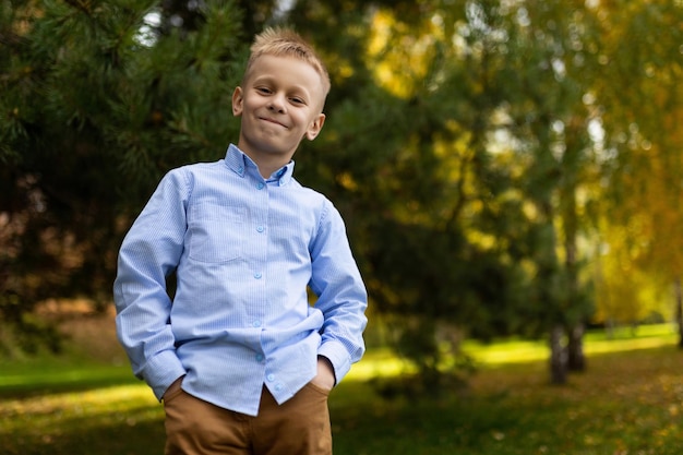 Retrato de um menino alegre em uma camisa azul em pé com as mãos nos bolsos contra o