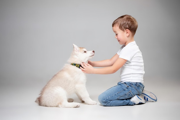 Retrato de um menino alegre se divertindo com o cachorrinho husky siberiano no chão do estúdio. O animal, amizade, amor, animal de estimação, infância, felicidade, cachorro, conceito de estilo de vida