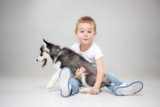 Retrato de um menino alegre se divertindo com o cachorrinho husky siberiano no chão do estúdio. o animal, amizade, amor, animal de estimação, infância, felicidade, cachorro, conceito de estilo de vida