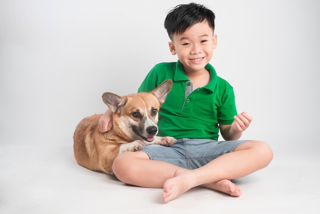 Retrato de um menino alegre se divertindo com o cachorro corgi galês no chão