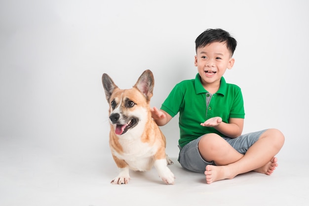 Retrato de um menino alegre se divertindo com o cachorro corgi galês no chão