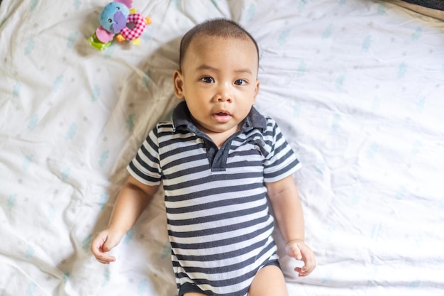 Foto retrato de um menino asiático de sorriso feliz relaxando olhando para a câmeracriança recém-nascida asiática bonita na cama em casa