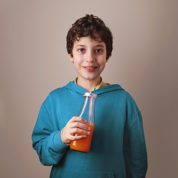 Retrato de um menino bebendo suco de laranja em uma garrafa com canudo