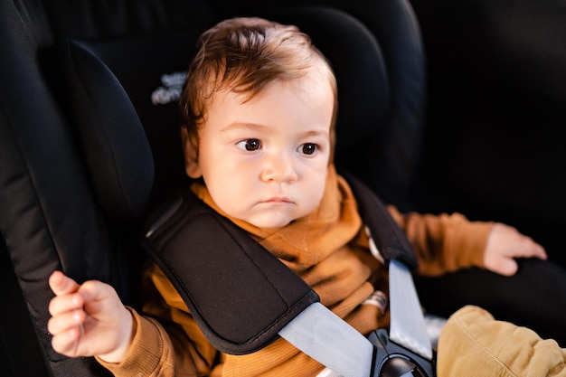 Retrato de um menino bonitinho sentado em um assento de carro preto preso com cintos de segurança