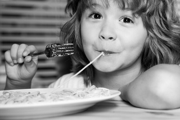 Retrato de um menino bonito comendo macarrão espaguete feche o rosto de crianças caucasianas closeup cabeça de criança engraçada