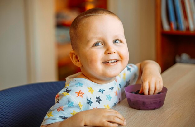 Foto retrato de um menino bonito comendo mirtilos em casa