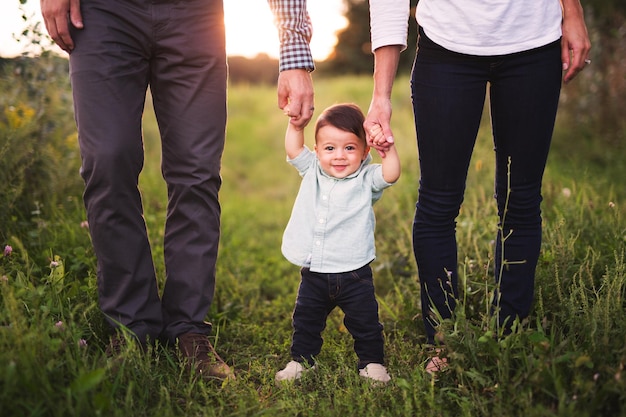Retrato de um menino bonito segurando as mãos dos pais enquanto está de pé na grama