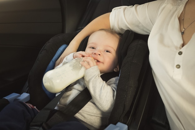 Retrato de um menino bonito sentado na cadeirinha do carro com a garrafa