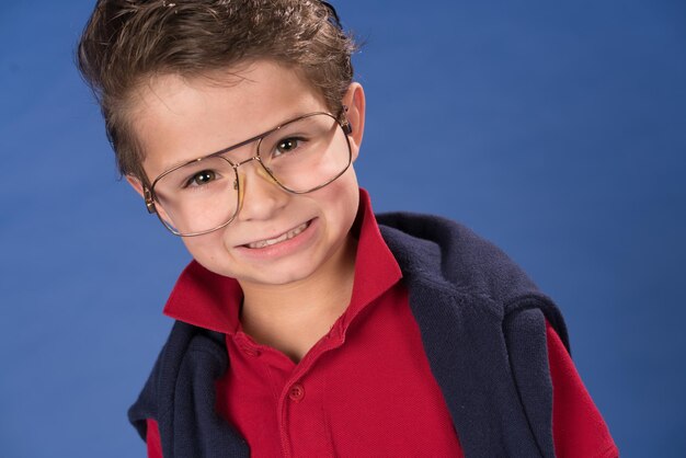 Foto retrato de um menino bonito sorridente usando óculos de pé contra um fundo azul