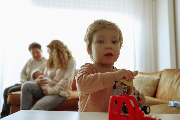 Retrato de um menino brincando com um brinquedo com a mãe e a avó no fundo