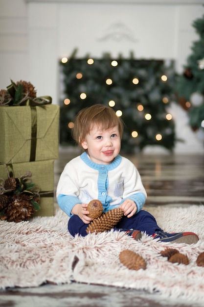 Retrato de um menino brincar com pinhas perto de uma árvore de Natal.