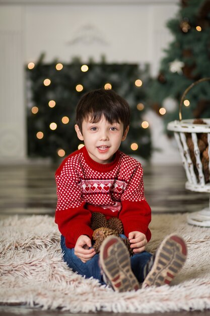 Retrato de um menino brincar com pinhas perto de uma árvore de Natal.