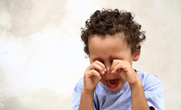Foto retrato de um menino cobrindo o rosto contra a parede