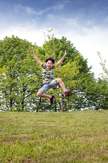 Foto retrato de um menino com os braços estendidos pulando contra árvores