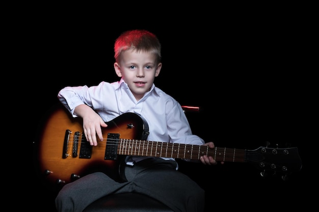 Retrato de um menino com uma guitarra elétrica, sentado em uma cadeira, isolado em um fundo preto