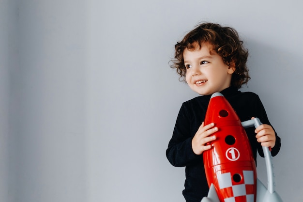 Retrato de um menino com uma nave espacial vermelha nas mãos em uma parede cinza