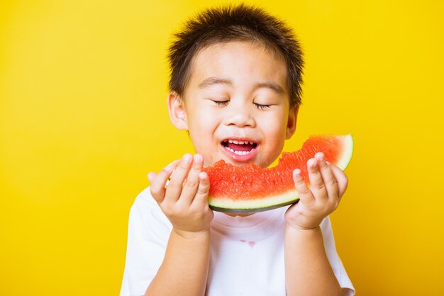 Foto retrato de um menino comendo frutas contra um fundo amarelo