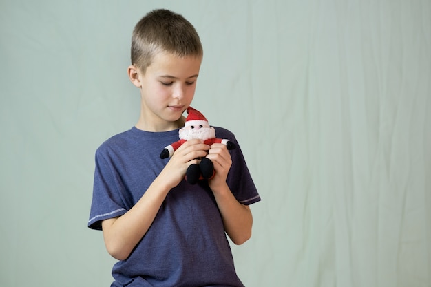 Retrato de um menino de criança brincando com um pequeno brinquedo de Papai Noel.