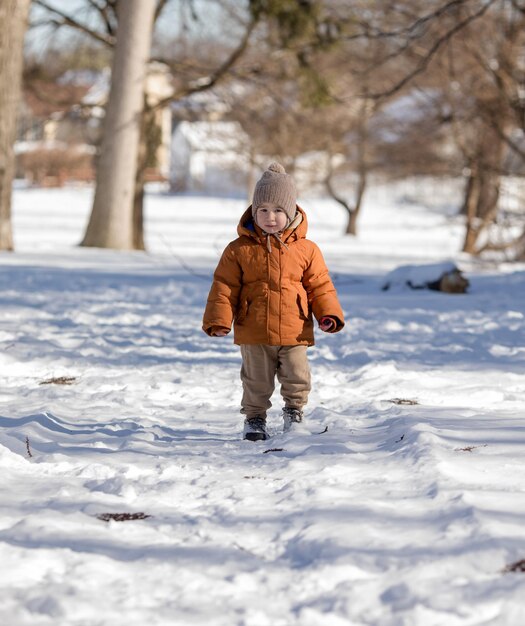 Retrato de um menino de dois anos de idade de pé na neve fresca no inverno jogando ao ar livre