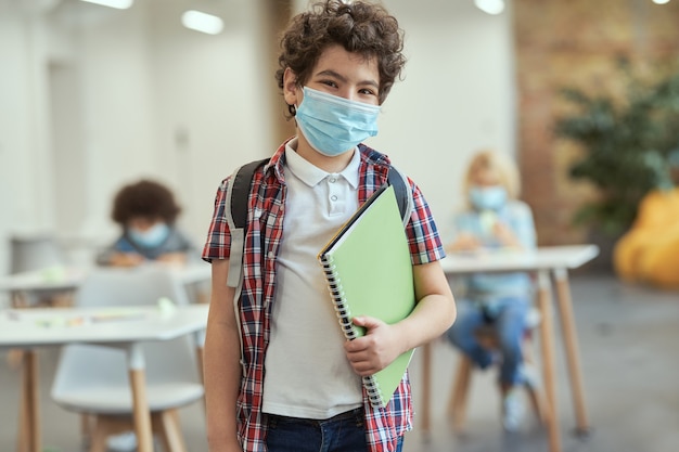 Retrato de um menino de escola alegre usando uma máscara para evitar a propagação de olhares cobiçosos