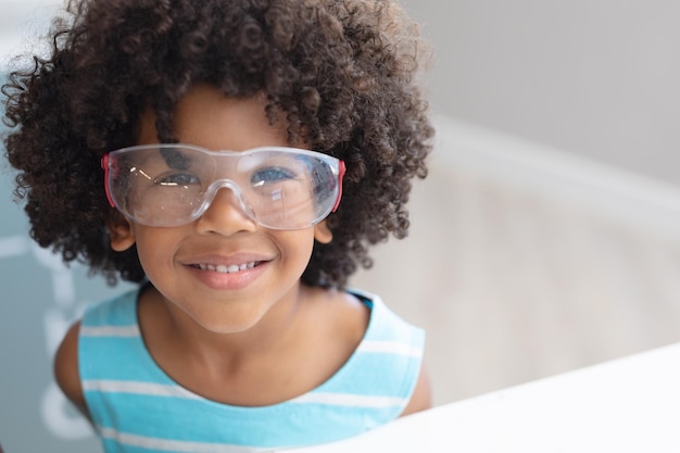 Retrato de um menino de escola primária afro-americano sorridente usando óculos de proteção em laboratório