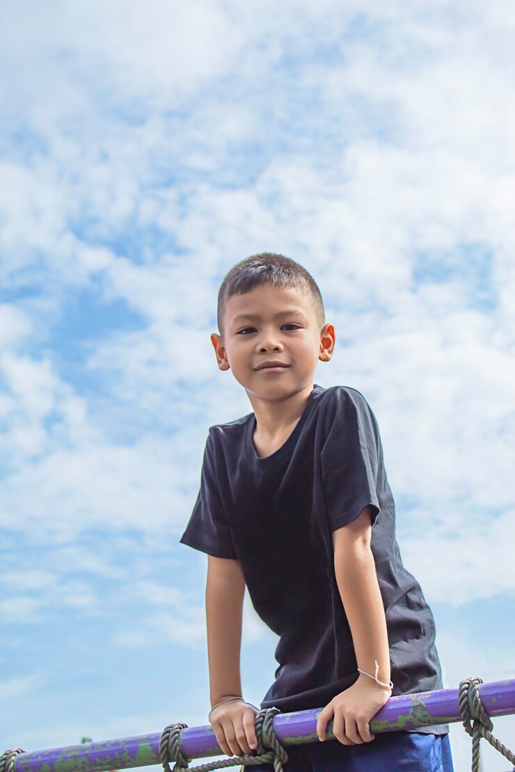 Foto retrato de um menino de pé junto a um corrimão contra o céu