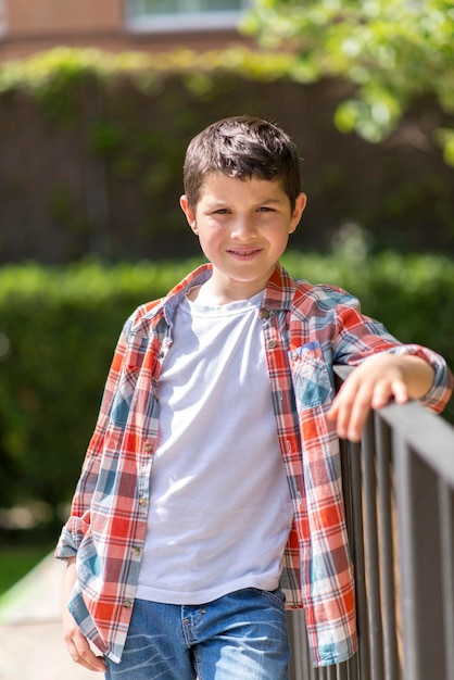 Foto retrato de um menino de pé perto de uma grade no parque