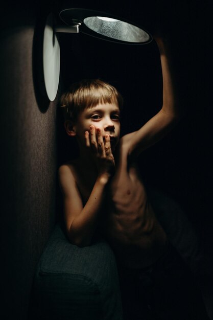 Retrato de um menino de pé sob uma luz iluminada em casa