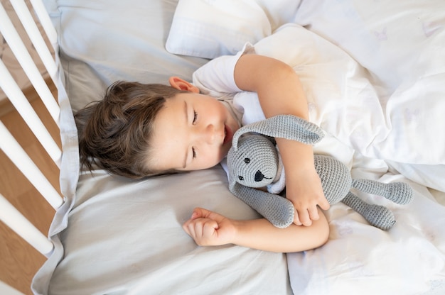 Retrato de um menino dormindo em uma cama branca, vista superior. Menino dormindo com coelho de malha. Foto de alta qualidade