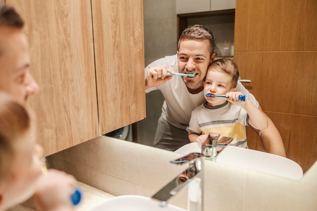 Retrato de um menino e seu pai escovando os dentes juntos em um banheiro