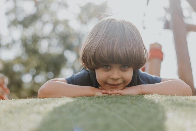 Retrato de um menino em uma camiseta azul, deitado na grama verde. criança está brincando no parque. atividades ao ar livre, estilo de vida. espaço para texto. Foto de alta qualidade