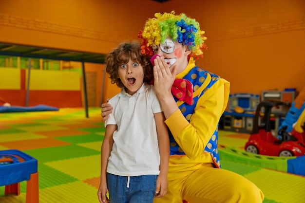 Retrato de um menino engraçado e um palhaço animador em um playground coberto