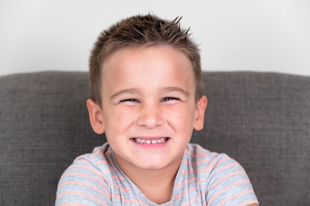 Foto retrato de um menino engraçado sorrindo e rindo olhando para a câmera sentada no sofá em casa conceito de uma infância feliz