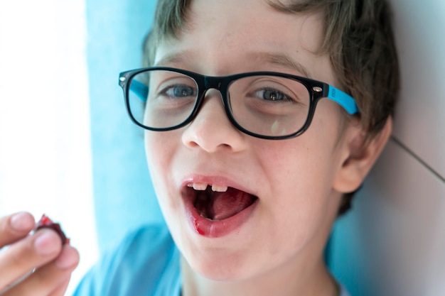 Retrato de um menino feliz com óculos que come cerejas e sorri Uma criança alegre em casa entre a família Uma infância feliz e despreocupada