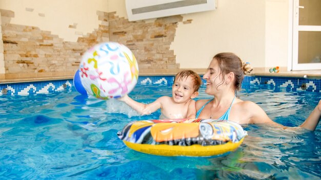 Retrato de um menino feliz rindo com uma jovem mãe brincando com uma bola de praia inflável colorida na piscina de um hotel resort de verão