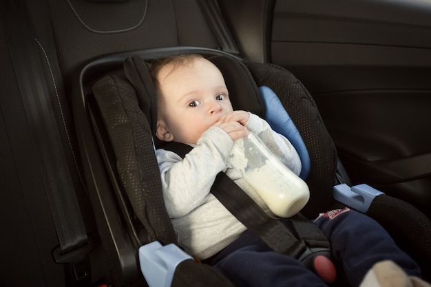 Retrato de um menino fofo bebendo leite na cadeirinha do carro