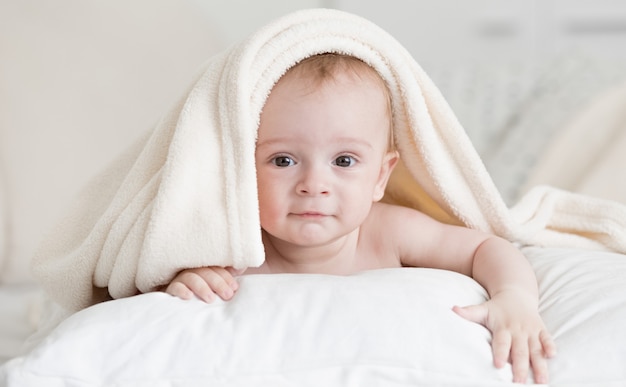 Retrato de um menino fofo deitado na cama, debaixo de uma toalha, após o banho